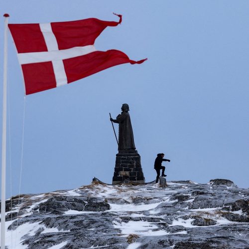 Um homem caminha enquanto a bandeira dinamarquesa tremula ao lado da estátua de Hans Egede antes...